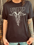 Black Phillip The Witch black t-shirt featuring a black and white illustration of Phillip with the word "Phillip" in large black letters outlined in white at the top, on a model.