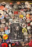 Rush Neil Peart RIP coozie featuring a black and white image of him on the drums with his name across the top and the dates "1952-2020" across the bottom in black and white text, photographed on a bunch of band button pins.