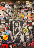 Thin Lizzy coozie featuring a black and white image of Phil Lynott playing guitar' photographed on top of a bunch of band pins.