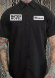 "Bates Motel" black work shirt featuring a patch with those words over the right breast pocket and a "Norman" name patch over the left breast pocket, photographed on a model in front of a metal gate background.