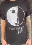 Front of Bauhaus Brighter Mornings black t-shirt featuring vol 1 album artwork in white, on a model against a metal gate background.