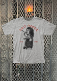 Light heather grey Bon Scott RIP t-shirt with an image of him singing and red text for 'Bon Scott' and '1946 1980' on a metal gate background.