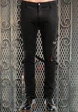 Male model wearing skinny leg fitted black pants with straps in the back and a zippered pocket on the left side knee area, against a metal gate background.
