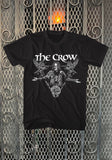 The Crow Eric Draven Triangle black t-shirt featuring the movie logo in white and a black and white image of Eric coming out of a triangle with two crows and a rose in the corners, displayed against a metal gate background.