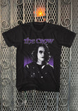 The Crow Purple Eric Draven black t-shirt featuring the movie logo in purple and a black and white image of Eric on a purple and black background, displayed against a metal gate background.