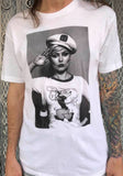 Debbie Harry of Blondie white t-shirt featuring a black and white image of her wearing a Popeye t-shirt while she is wearing a captain's hat and saluting, on a model against a metal gate background.