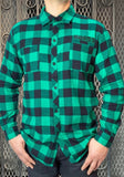 Front of Franken Monster flannel green and black button down long sleeve shirt featuring the word 'Monster' embroidered in black and green above the left chest pocket, on a model in front of a metal gate background.