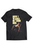 Iggy Pop I Wanna Be Your Dog black t-shirt featuring large yellow text 'Now I Wanna Be Your Dog' above an image of Iggy crawling on all fours with his tongue sticking out, displayed on a white background.