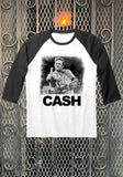 Johnny Cash Finger white raglan t-shirt with black 3/4 sleeves featuring a black and white image of him holding up his middle finger while on guitar and 'Cash' in large black text under the image, displayed against a metal gate background.