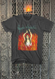 Front of Janes Addiction Ritual black t-shirt featuring burning imagery from the album artwork and the band logo in green text, displayed on a metal gate background.