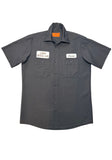 Black button down work shirt featuring an embroidered patch with a white background and black script 'Jason' on the left breast and an embroidered patch with a white background and text stylized in wood planks 'Camp Crystal Lake' on the right breast, on white background.