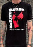 Black Kulture Vulture logo t-shirt featuring the red store logo with white letters for 'Kulture Vulture' and 'French Quarter NOLA', photographed on a model in front of a metal gate background.