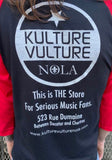 Back of Kulture Vulture black raglan t-shirt with red 3/4 sleeves featuring the circular store logo and text "This is the store for serious music fans. 523 Rue Dumaine Between Decatur and Chartres" along with the website URL.