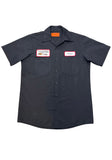 Black button down work shirt featuring an embroidered patch with a white background, red trim and black script 'Leatherface' on the left breast and an embroidered patch with a white background, red trim and text 'Texas Chainsaw Mfg. Corp.' along with an image of a chainsaw on the right breast, on a model against a white background.