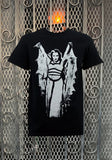Lily Munster Batwing black t-shirt featuring a black and white image of her wearing a batwing cape and arms outstretched, displayed on a metal gate background.