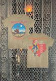 A vintage-style Iron Maiden graphic T-shirt shown in front and back views, laid flat against a decorative metal gate background. The front features the band name in red above a circular desert scene with Eddie and the text 'Texas 1982'.