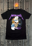 Front of Metallica Damaged Justice black t-shirt featuring skull artwork from the tour, displayed on a metal gate background.