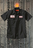 Black work shirt featuring a name patch that says 'M. Myers' on the left chest and patch with 'Haddonfield Memorial' on the right chest, displayed on a metal gate background.