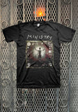 A black short-sleeve graphic t-shirt featuring the band Ministry and their 'The Great Devourer' album artwork, displayed flat against a decorative metal mesh background.
