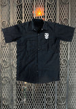 Front of Misfits Crimson Ghost black button down short sleeve work shirt featuring a white image of the crimson ghost above the left chest pocket, displayed on a metal gate background.
