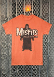 Misfits Crimson Ghost Halloween orange t-shirt featuring a large band logo and the word Halloween in white letters on top of a black and white Crimson Ghost figure illustration, displayed on a metal gate background.