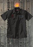 Black Mortician work shirt featuring a name patch that says 'Mortician' on the left chest and a black and red coffin shaped patch with a cross on the right chest, displayed on a metal gate background.