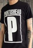 Portishead Classic Logo black t-shirt featuring their band name and large P logo in white, on a model against a metal gate background.
