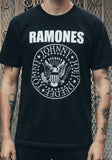 The Ramones Classic Logo black t-shirt featuring the band name in large white text above the circular logo design, on a model against a metal gate background.