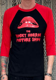Rocky Horror black raglan t-shirt with bright red 3/4 sleeves featuring the large lips logo and the words 'The Rocky Horror Picture Show' in red blood dripping text, on a model against a metal gate background.