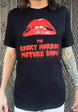 Rocky Horror black t-shirt featuring the large lips logo and words 'The Rocky Horror Picture Show' in large red blood dripping text, on a model in front of a metal gate background.