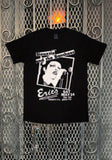 A black short-sleeve graphic T-shirt hanging against a metal mesh gate background. The shirt features a large white print with a portrait of Siousxie singing and text reading 'Siousxie and the Banshees' and 'Eric's'.