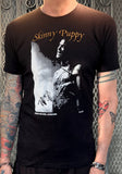 Skinny Puppy Greyhound London black t-shirt featuring artwork from the historic show at the Greyhound, on a model against a metal gate background.