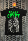 Tales from the Crypt More Comics black t-shirt featuring a black and white image of zombie hands along with the text 'Tales from the Crypt' in bright green above the image, displayed against a metal gate background.