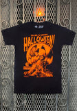 Tales from the Crypt Halloween Pumpkin black t-shirt featuring an orange image of a zombie coming out of a jack-o-lantern along with the text 'Tales from the Crypt' in orange above the image, displayed against a metal gate background.