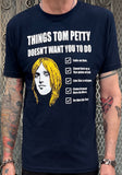 Tom Petty navy t-shirt featuring a drawing of his head and a checklist of "Things Tom Petty Doesn't Want You to Do" such as "Fade on Him" and "Live Like a Refugee", photographed on a model in front of a metal gate background.