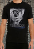Willie Nelson Dripping Springs 1973 black t-shirt featuring a black and white image of Willie wearing a 'shotgun willie' t-shirt along with text 'Willie Nelson Dripping Springs Texas 1973', on a model against a metal gate background.