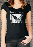 A woman wearing a black short-sleeve t-shirt with a white Bauhaus Bella Lugosi graphic print on the front, set against a metal gate background.
