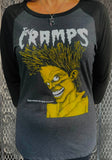 A person wearing a dark heather gray and black raglan t-shirt featuring a large yellow and white graphic of the band The Cramps with their Bad Music for Bad People design.