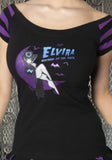 Elvira Mistress of the Dark black boatneck t-shirt with purple striped short sleeves featuring a graphic of Elvira reclining on a purple crescent moon with several bats flying around the text "Elvira Mistress of the Dark", photographed on a model in front of a metal gate background.