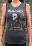 Heather grey Halloween Spanish movie poster tank top featuring a black, white, and orange image of Michael Myers holding a knife and Spanish text that says 'La Noche De Halloween, todo el mundo tiene derecho a un buen susto, La Noche Que Llegó A Casa!', on a model against a metal gate background.