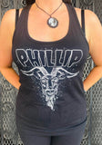 A woman wearing a black racerback tank top with a white graphic that reads 'PHILLIP' above a goat head illustration, standing in front of a metal gate.