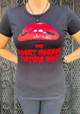 Rocky Horror Picture Show black t-shirt featuring the red lips and name from the movie artwork, photographed on a model in front of a metal gate background.