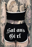 Back of black Satan's Girl shorts featuring the words 'Satan's Girl' in white lettering across the back, on a metal gate background.