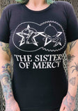 Sisters of Mercy black t-shirt featuring the classic gears logo and band name in white, photographed on a model in front of a metal gate background.