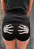 Black fitted shorts with a white skeleton hand graphic on the back on both sides, shown on a model from behind.