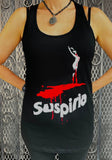 Suspiria black tank top featuring the movie artwork and name in red and white, photographed on a model in front of a metal gate background.
