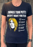 Tom Petty navy t-shirt featuring a drawing of his head and a checklist of "Things Tom Petty Doesn't Want You to Do" such as "Fade on Him" and "Live Like a Refugee", photographed on a model in front of a metal gate background.