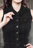 Black denim cropped women's vest with 6 silver tone buttons down the front, two buttoned front breast pockets, and a small skull and crossbones logo on the waist, on a metal gate background.