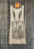 Off white racerback tank top featuring illustration imagery in black showing a witch walking with a broom in her hand along with a skeleton and a goat, photographed flat on a metal gate background.