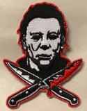 Close-up of Halloween Movie Franchise embroidered patch featuring Michael Myers face in black-and-white with a red outline, positioned above two crossed knives with blood dripping and outlined in red.
